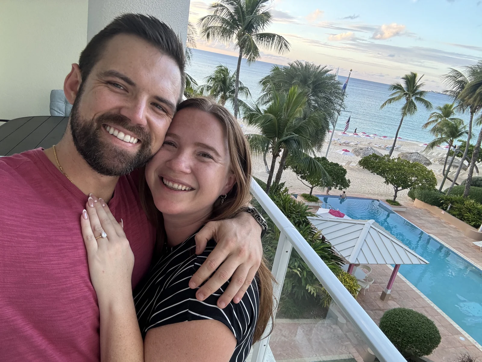 Gem and Bill cheek to cheek just after the yes — the ring catching the light, palms and pool below